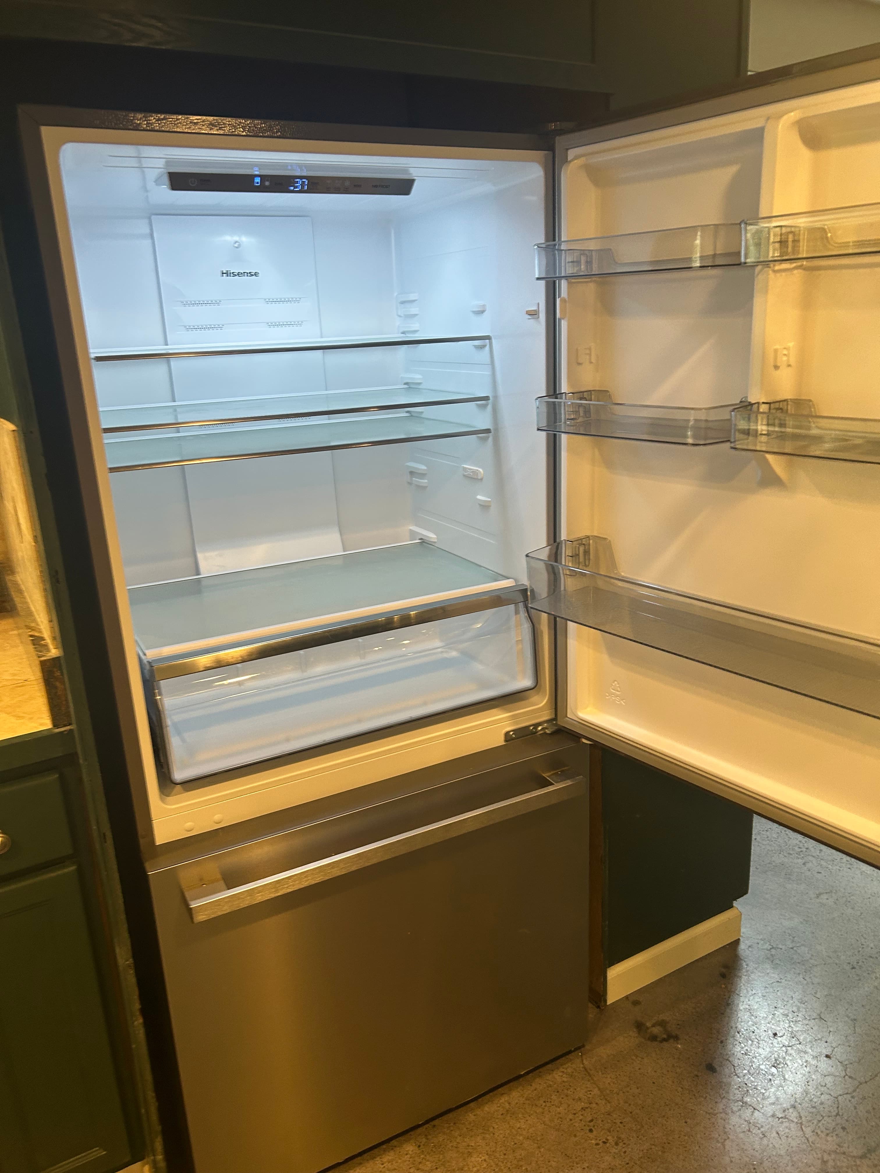 Open Hisense stainless steel refrigerator with empty glass shelves and bright interior lighting.